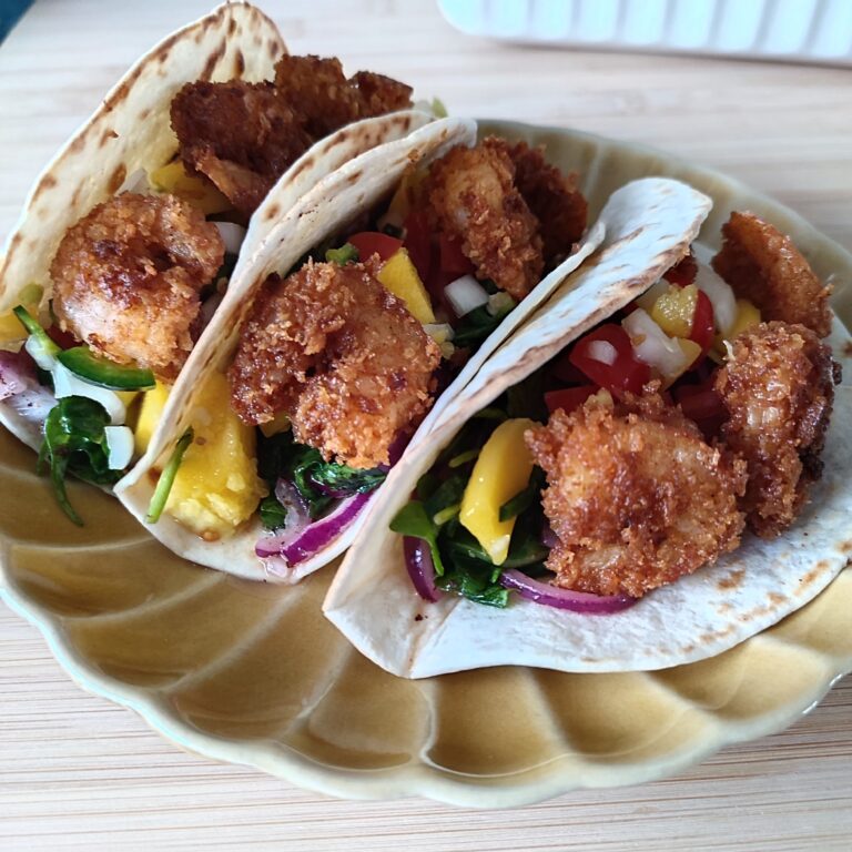 Crispy Shrimp Tacos with Spicy Mango Salsa on a scallop patterned ochre plate on a working surface