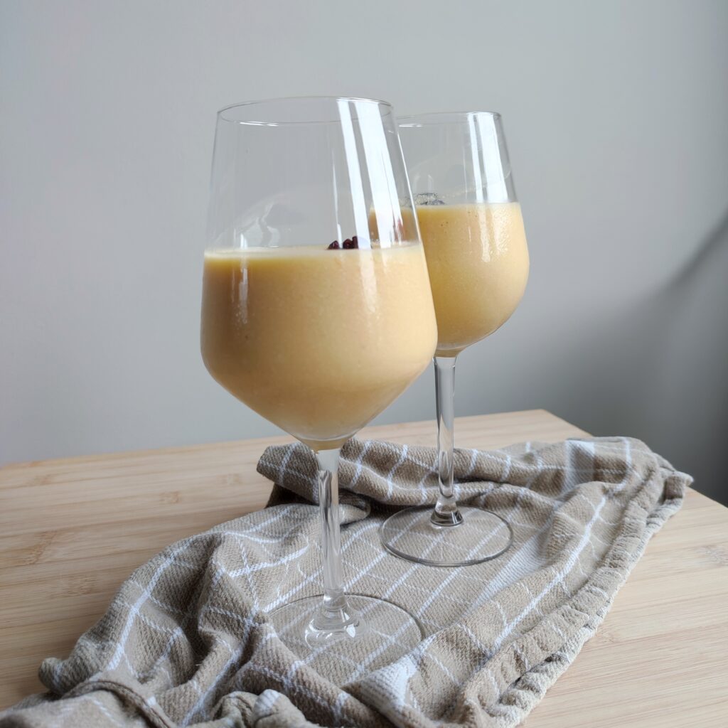 B roll 1: Rosé Mango Piña Colada in two wine glasses topped with one whole cherry on a warm taupe checkered fabric on a working surface side shot