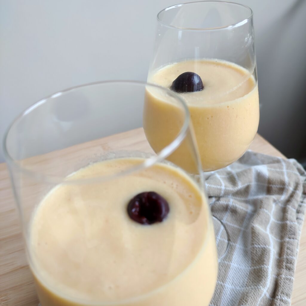 B roll 2: Rosé Mango Piña Colada in two wine glasses topped with one whole cherry on a warm taupe checkered fabric on a working surface side close up shot