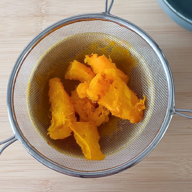 Peeled roasted pumpkin pieces on a strainer with a small yellow patterned bowl underneath