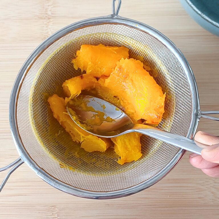 Pressing peeled roasted pumpkin pieces through the strainer with a small yellow patterned bowl underneath