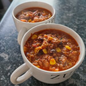 Chilli Con Carne served in a two white coloured soup bowl with black writing on the side and the bowls are placed on a blue and grey patterned kitchen counter