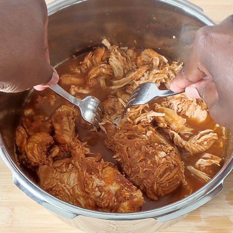 Shredding or 'pulling' the chicken breast fillet with two forks in the pressure cooker