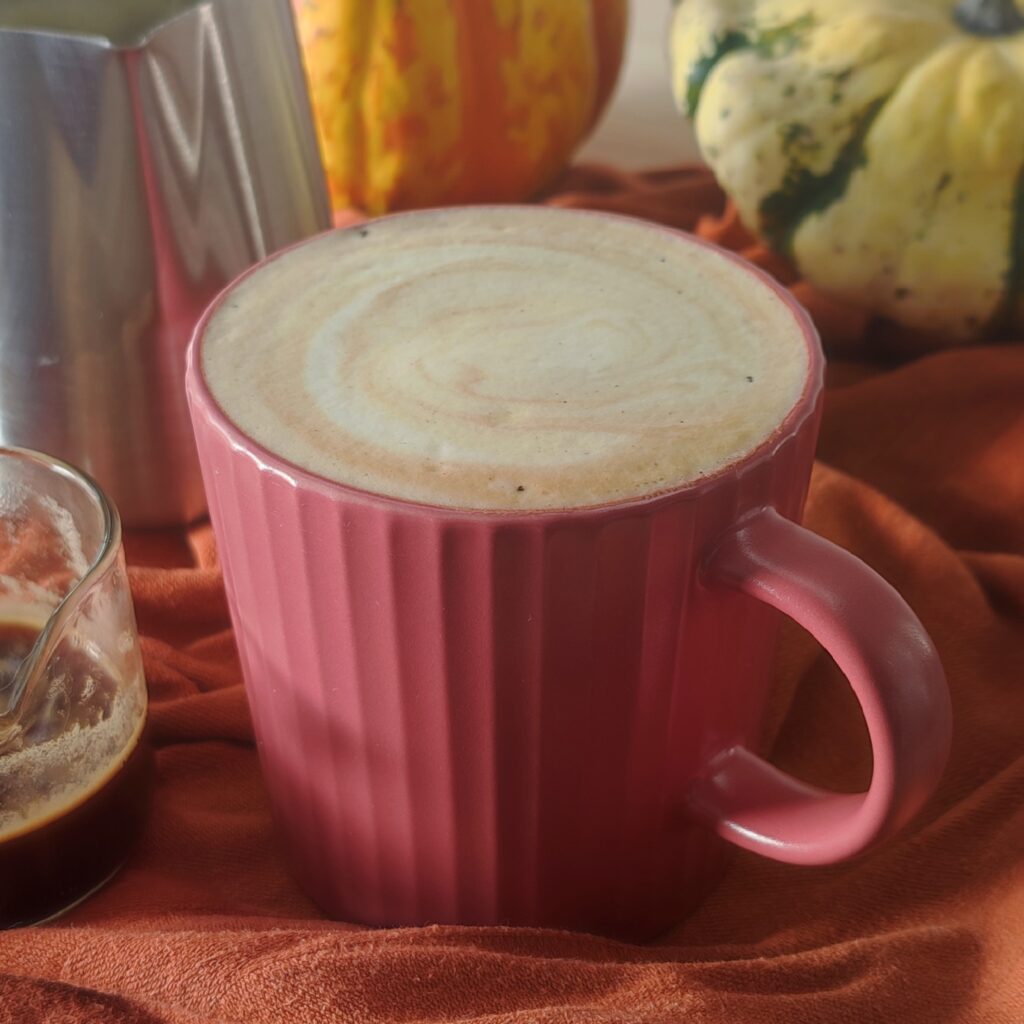 B roll 1: Dirty Pumpkin Spice London Fog Latte accompanied by a shot of espresso in a shot glass with a stainless steel mug and pumpkins on burnt orange fabric