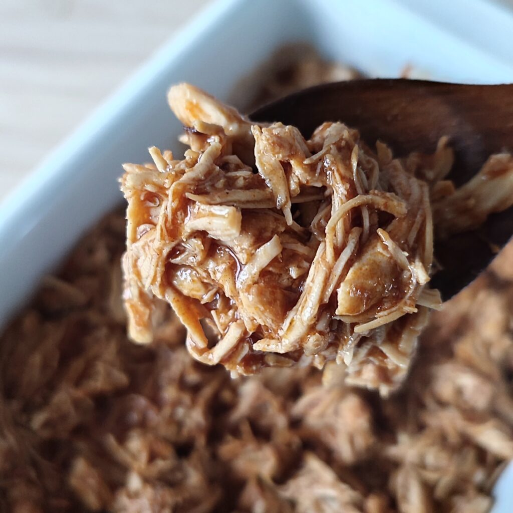 B roll 2: Instant One Pot Spicy BBQ Pulled Chicken scooped on a spatula with the rest of it in a white casserole dish in the background