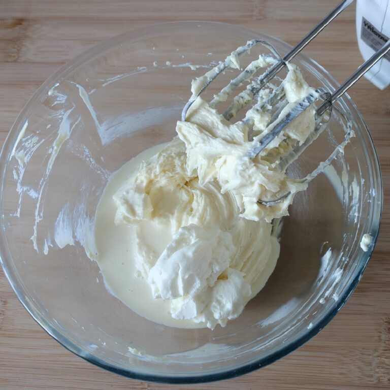 Adding sour cream and heavy cream to cream cheese mixture in a large clear bowl