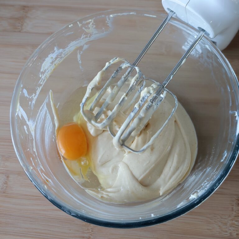 Adding a whole egg to cream cheese mixture in a large clear bowl