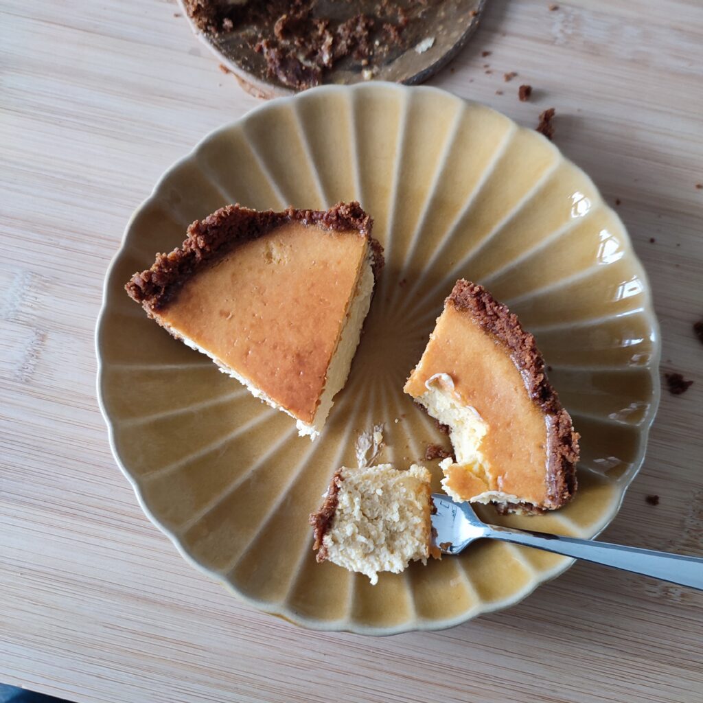 Two slices of Rustic Airfryer Pumpkin Spiced Cheesecake on a ochre coloured ribbed plate with one slice half eaten and a scoop pf cheesecake is on a small fork resting on the plate