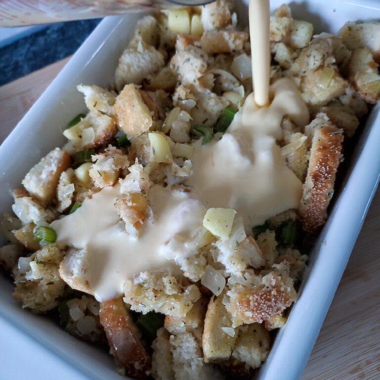 Adding egg + heavy milk mix to the stuffing in a white coloured rectangular casserole dish