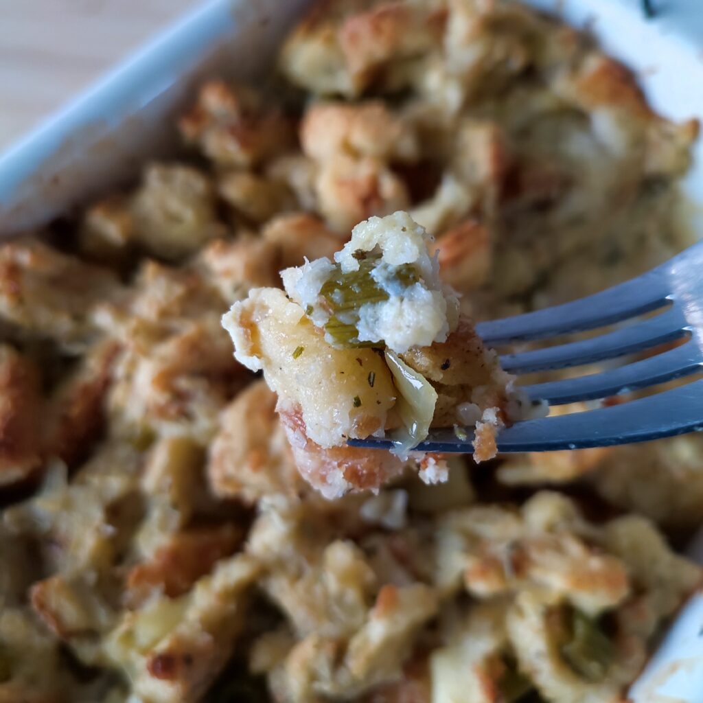 B shot 2 : A forkful of Easy Christmas Buttery Apple Herb Stuffing with the rest in the background in a white coloured rectangular casserole dish