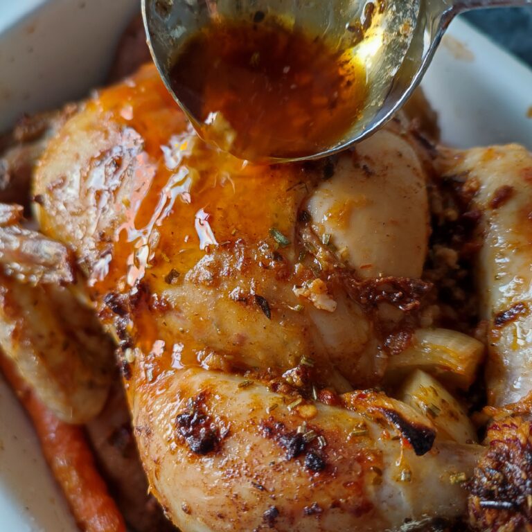 Basting the Christmas Roast Chicken midway while baking with it's own drippings in a white rectangular casserole dish