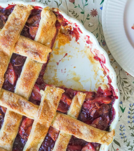 A closeup of the Apple Cherry Almond Pie with a slice missing and the missing slice is on a white plate opposite it