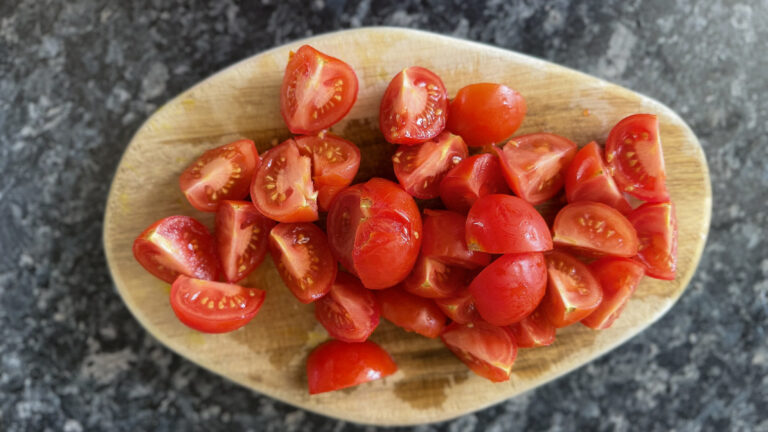 Chopped cherry tomatoes on a chopping board on a blue grey black coloured kitchen top