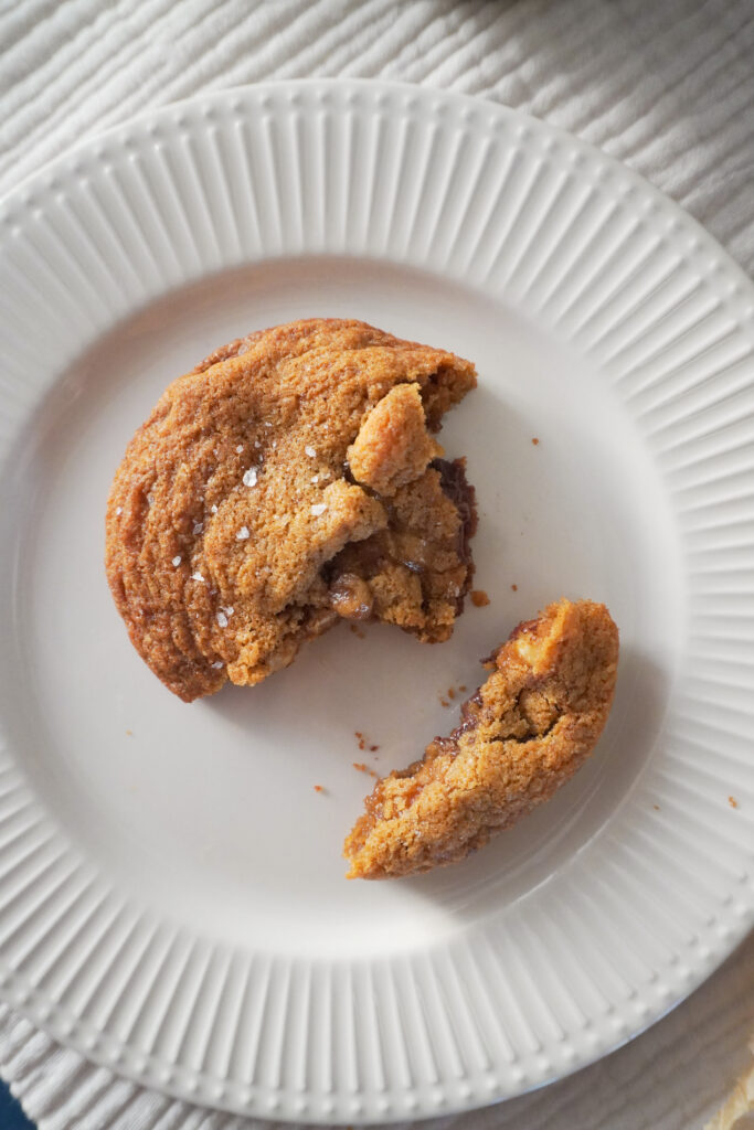 B Roll 1: A half eaten Nutella Cardamom Chocolate Chip Cookie on a white plate with ribbed edges