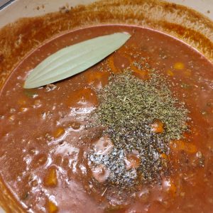 Adding dried herbs to the ragu in Dutch oven