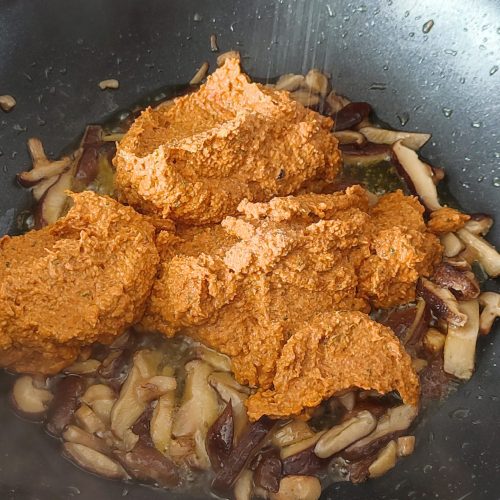 Adding red pesto and salt in the pan on the stove