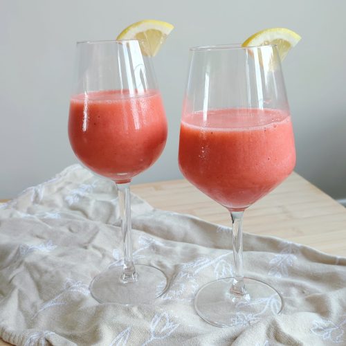 Pink Sgropinno in two wine glasses with a wedge of quartered lemon on the rims standing on taupe coloured fabric on a working surface fullshot ready to be served