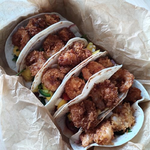 Ready to serve Crispy Shrimp Tacos with Spicy Mango Salsa in a off white casserole dish that is lined with crinkled up parchment paper on a working surface