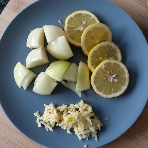 Prepped onion chunks, lemon slices and minced garlic on a medium blue plate