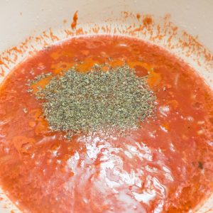 Adding canned crushed tomatoes, water, salt, sugar, Worcestershire sauce, dried basil, and black pepper into the casserole dish