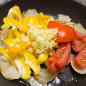 Adding bell pepper, ginger, garlic and tomato to sauteed onions in a pan