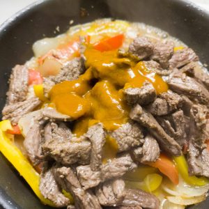 Adding lomo saltado sauce and browned beef to the rest in the pan