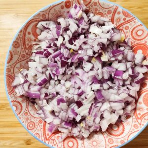 Chopped onions in a red patterned bowl on a working surface