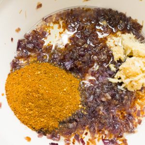 Adding berbere spice and ginger garlic paste to caramelised onions in a casserole pan