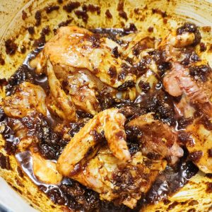 Adding and frying chicken to the spice mixture in a casserole pan