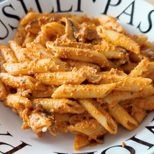 Pasta Pesto Rosso with Shiitake Mushrooms on a white plate with black lettering ready to be served