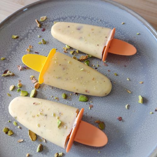 Ready to serve Mango Cardamom Pistachio Popsicles topped with roasted pistachios on a large gray plate